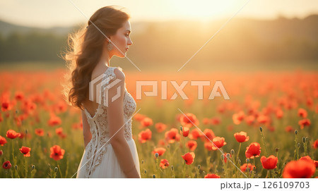 Woman in elegant dress stands in poppy field during sunset, creating a serene moment in nature's beauty 126109703