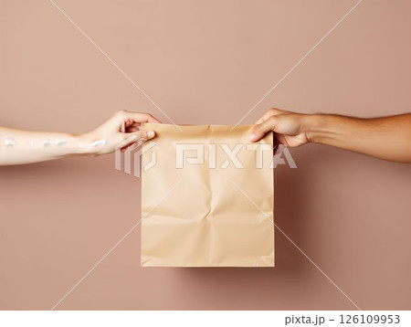 Two hands exchanging a brown paper bag against a neutral background in a close-up view 126109953