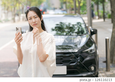 車の前でスマホを見て悩む女性 車の前でスマホを見て悩む女性 126110213