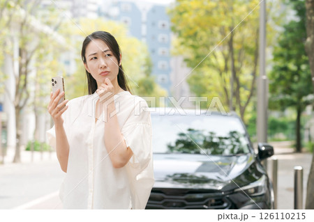 車の前でスマホを見て悩む女性 車の前でスマホを見て悩む女性 126110215