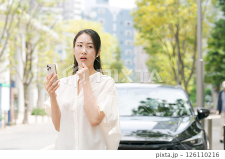車の前でスマホを見て悩む女性 車の前でスマホを見て悩む女性 126110216
