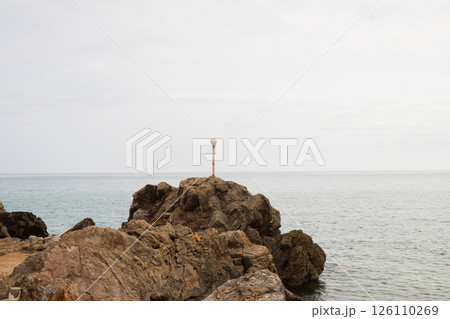 Solitary white pole on rocky seashore against overcast sky 126110269