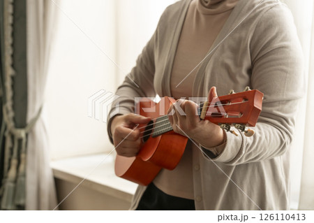窓辺でウクレレを弾くシニア女性 126110413