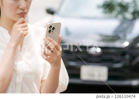 車の前でスマホを操作する若い女性 126110474