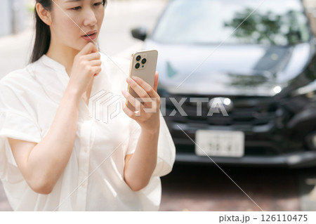 車の前でスマホを操作する若い女性 126110475