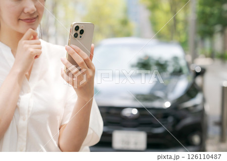 車の前でスマホを操作する若い女性 126110487
