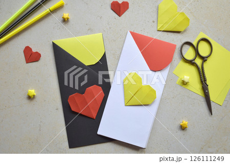 Handmade Crafting Process of a DIY Greeting Card with Origami Paper Hearts, Glue Application, Creative Stationery, Scissors, and Colorful Decorative Elements on a Light Artistic Background 126111249
