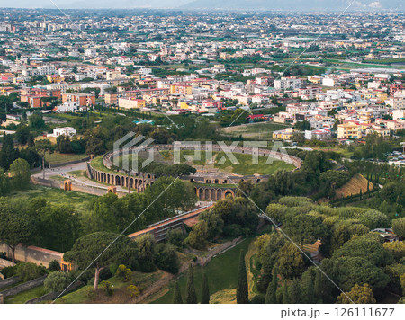 Aerial image of the ancient Pompeii amphitheater, surrounded by greenery, modern buildings, and a mountainous horizon in the background. Aerial image of the ancient Pompeii amphitheater, surrounded by greenery, modern buildings, and a mountainous horizon in the background. 126111677