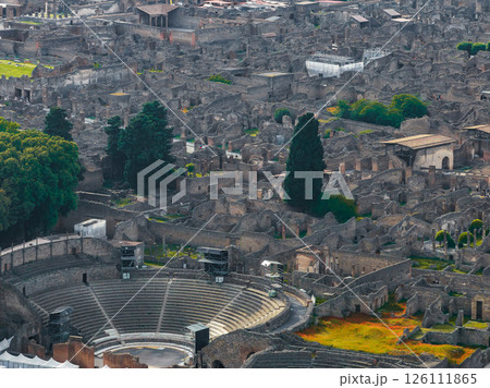 Aerial view of Pompeii ruins in Italy featuring the amphitheater with semi circular seating, surrounded by ancient streets, buildings, and greenery. Aerial view of Pompeii ruins in Italy featuring the amphitheater with semi circular seating, surrounded by ancient streets, buildings, and greenery. 126111865