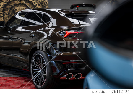 Black Lamborghini Urus parked indoors on red and black checkered floor, showcasing taillights, quad exhaust pipes, alloy wheels, and lion motif wall. 126112124