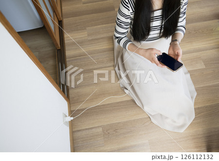 Woman sitting on floor while charging smartphone 126112132