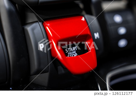 Detailed view of a Lamborghini Urus engine start button under a red flip cover, surrounded by black and metallic accents with gear indicators visible. Detailed view of a Lamborghini Urus engine start button under a red flip cover, surrounded by black and metallic accents with gear indicators visible. 126112177