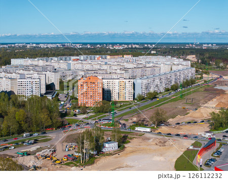 Construction activity with machinery and materials in Riga, Latvia, set against residential blocks, greenery, and a clear blue sky. Construction activity with machinery and materials in Riga, Latvia, set against residential blocks, greenery, and a clear blue sky. 126112232