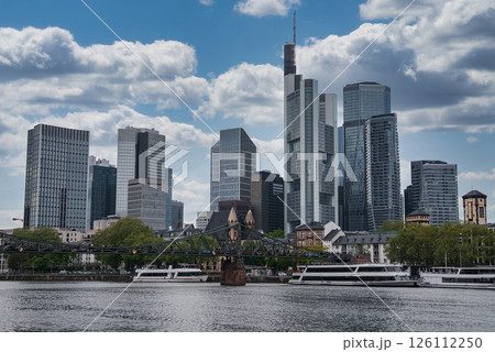 Modern skyscrapers, including Commerzbank Tower, rise above Frankfurt. The River Main and Eiserner Steg bridge are framed by trees and mixed architecture. 126112250
