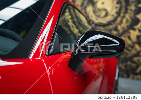 Side mirror and door of a red 2025 Porsche 911 GT3 922 with glossy black accents. Reflections and a golden abstract mural enhance the modern design. Side mirror and door of a red 2025 Porsche 911 GT3 922 with glossy black accents. Reflections and a golden abstract mural enhance the modern design. 126112288