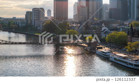 Aerial view of Frankfurt, Germany, featuring the Main River, Eiserner Steg bridge, modern skyscrapers, historic buildings, and docked boats in sunlight. Aerial view of Frankfurt, Germany, featuring the Main River, Eiserner Steg bridge, modern skyscrapers, historic buildings, and docked boats in sunlight. 126112337
