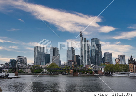 Skyline of Frankfurt, Germany, featuring Commerzbank Tower, the River Main, and Eiserner Steg bridge, with modern and traditional architecture under an overcast sky. 126112378