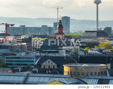 Aerial view of Frankfurt, Germany, showing Katharinenkirche, Europaturm, modern high rises, construction cranes, and green trees under soft daylight. Aerial view of Frankfurt, Germany, showing Katharinenkirche, Europaturm, modern high rises, construction cranes, and green trees under soft daylight. 126112403