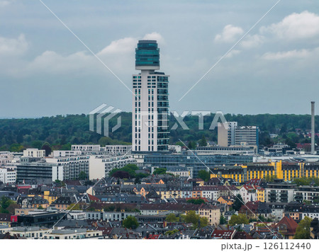 Aerial view of Frankfurt, Germany, highlighting a modern high rise with a cylindrical glass top, surrounded by urban housing, greenery, and a cloudy sky. Aerial view of Frankfurt, Germany, highlighting a modern high rise with a cylindrical glass top, surrounded by urban housing, greenery, and a cloudy sky. 126112440