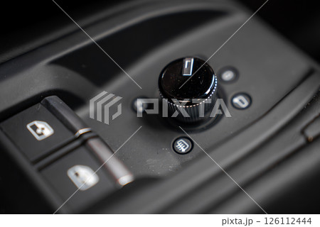 Close up view of a car's interior control panel featuring a black rotary knob, buttons for various functions, and a modern, high end design. 126112444
