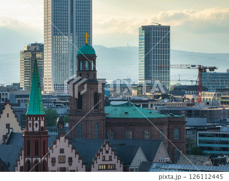 Frankfurt cityscape featuring St. Paul's Church with its green dome, traditional gabled buildings, modern skyscrapers, and a construction crane under a cloudy sky. 126112445