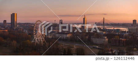Serene sunrise over Riga, Latvia, featuring the Vansu Bridge, Z Towers, Riga Ferris Wheel, and the Daugava River reflecting warm morning light. Serene sunrise over Riga, Latvia, featuring the Vansu Bridge, Z Towers, Riga Ferris Wheel, and the Daugava River reflecting warm morning light. 126112446
