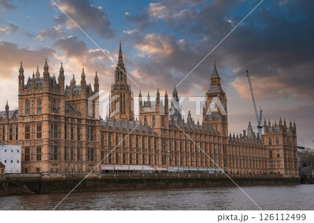The Palace of Westminster and Big Ben in London, England, with Gothic Revival architecture, a dramatic sky, and the River Thames in the foreground. 126112499