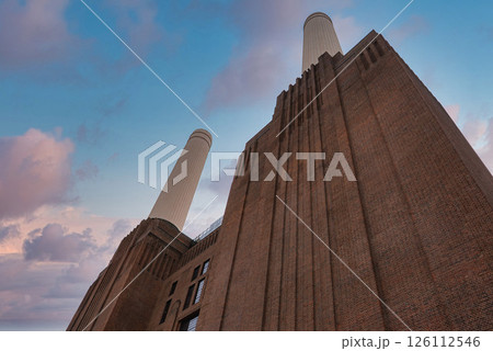 The iconic Battersea Power Station in London features Art Deco architecture, four white chimneys, and a vibrant sky with pink and blue hues. 126112546