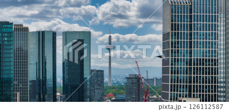 Frankfurt, Germany, featuring the Europaturm in the background, modern skyscrapers with glass facades, construction cranes, and a partly cloudy sky. 126112587