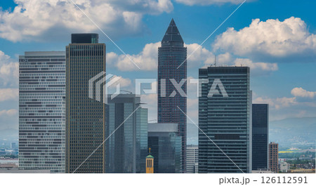Frankfurt's skyline features the Messeturm with its pyramid roof, modern high rises like the Trianon, a church with a golden cross, and a cloudy sky. 126112591