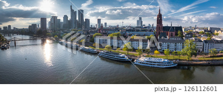 Aerial view of Frankfurt, Germany, featuring the Main River, Commerzbank Tower, Frankfurt Cathedral, Eiserner Steg bridge, and docked boats. 126112601
