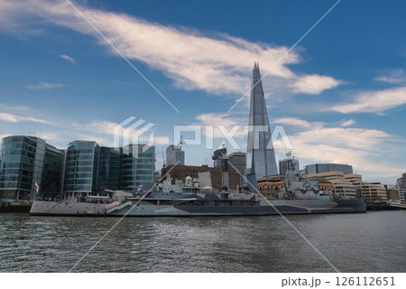 View of the Shard skyscraper towering over modern buildings, with HMS Belfast moored on the River Thames, showcasing London's mix of history and architecture. 126112651