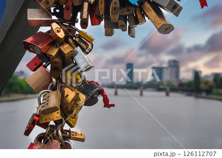 Colorful love locks adorn a metal structure, with the Main River, a bridge, and modern high rise buildings in Frankfurt, Germany, in the background. Colorful love locks adorn a metal structure, with the Main River, a bridge, and modern high rise buildings in Frankfurt, Germany, in the background. 126112707