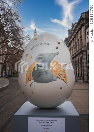 Outdoor display of a painted egg sculpture featuring an elephant under a crescent moon, with London architecture and a clock tower spire in the background. Outdoor display of a painted egg sculpture featuring an elephant under a crescent moon, with London architecture and a clock tower spire in the background. 126112790