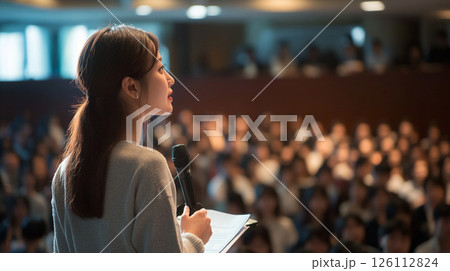 大勢の聴衆の前でプレゼンをしている女性 大勢の聴衆の前でプレゼンをしている女性 126112824