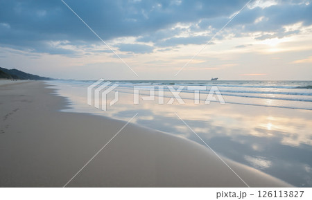 A quiet, empty beach at low tide, with the vast sky above reflecting the colors of the ocean. The smooth, 126113827