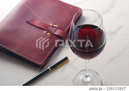 赤ワインを飲みながら、ワインレッドの革のシステム手帳に日記をつけているイメージ 126113917