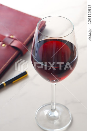 赤ワインを飲みながら、ワインレッドの革のシステム手帳に日記をつけているイメージ 赤ワインを飲みながら、ワインレッドの革のシステム手帳に日記をつけているイメージ 126113918