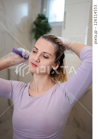 Woman dyeing her hair purple with a brush in bathroom Woman dyeing her hair purple with a brush in bathroom 126114553