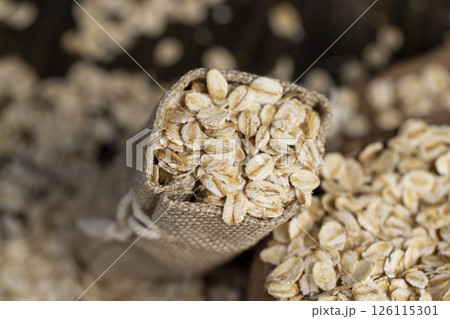 one linen bag with flakes for making porridge, scattered dry cereal flakes from oats, flattened, steamed and dried, closeup 126115301