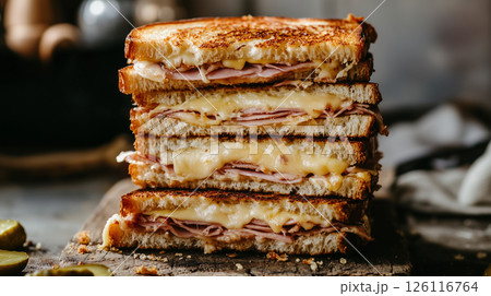 Stack of toasted Cuban sandwiches on rustic wooden board with melted cheese, ham, pickles, and mustard, warm light and cozy kitchen background, comfort food scene 126116764