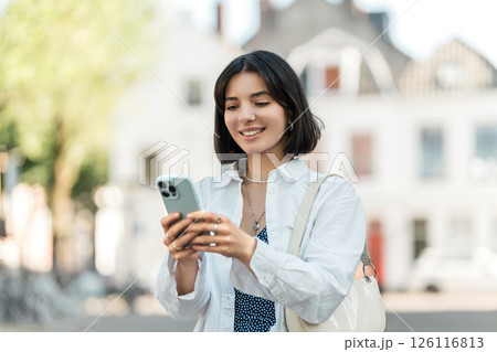 Waiting for directions to load, a stylish young woman of mixed heritage scrolls her phone against a charming European backdrop 126116813