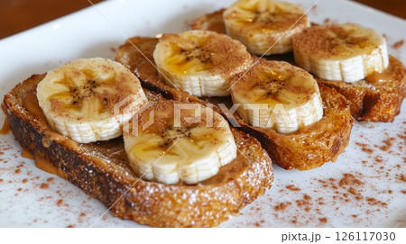 Healthy breakfast featuring banana slices on creamy peanut butter toast. Fresh, natural ingredients create a simple yet delicious morning meal in rustic style. 126117030