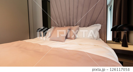 A cozy modern hotel bed with pastel bedding, soft pillows and elegant lighting setup 126117058