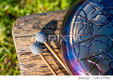 Steel tongue drum and mallets resting on a wooden bench. Concept of sacred stillness, sound meditation, and harmony with nature 126117992