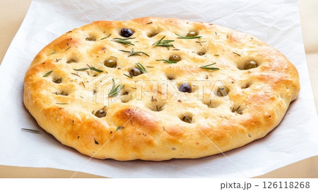 Fresh sourdough focaccia with olives and rosemary on parchment, golden crust, top view, rustic baking scene, natural daylight, simple and artisanal look 126118268