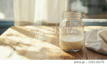 Active sourdough starter in a glass jar with visible fermentation bubbles, rustic wooden background and natural light, ideal for slow food and healthy baking visuals. 126118270