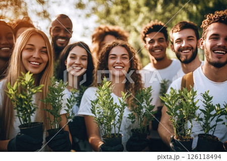 Group of diverse individuals smiling while holding young plants in pots, standing outdoors in a sunny environment, showcasing teamwork and environmental awareness 126118494