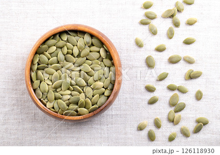 Pepitas, hulled pumpkin seeds, in a wooden bowl, on linen. Raw, dried squash seeds, fruits of Cucurbita, light green after the husk is removed, and used as snack, garnish or as an ingredient. Photo 126118930