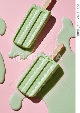 Green pistachio mint melting ice cream on a stick, pink background, vertical trending magazine photo 126119578